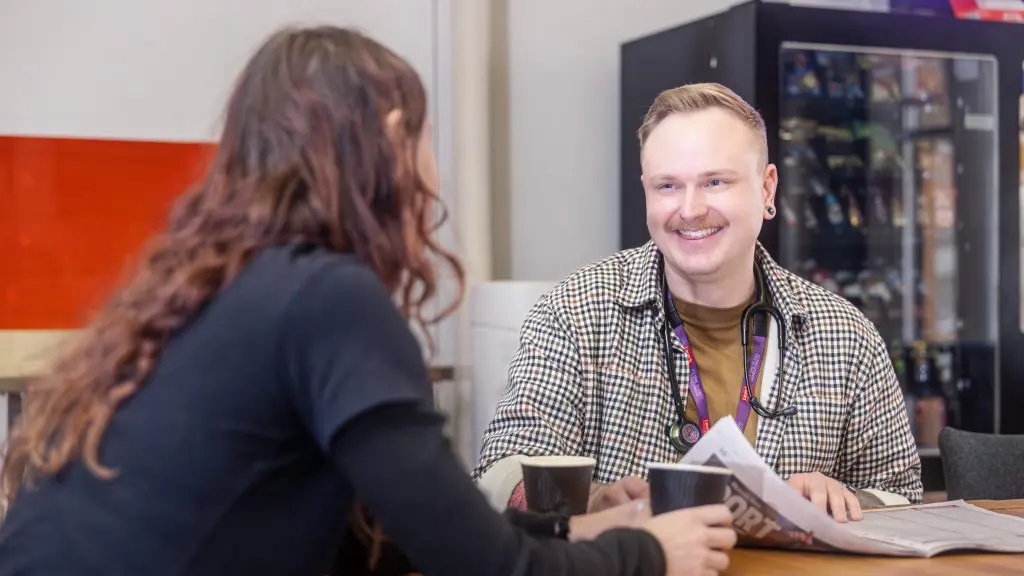 Community nurse is smiling, sitting at a table with a client.